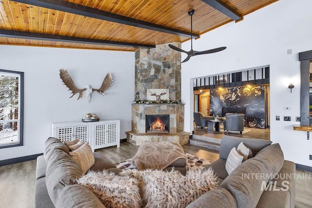 living room featuring hardwood / wood-style flooring, beam ceiling, a stone fireplace, and wood ceiling