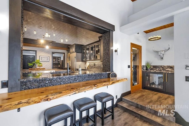 kitchen with stainless steel refrigerator, dark wood-type flooring, tasteful backsplash, beamed ceiling, and kitchen peninsula