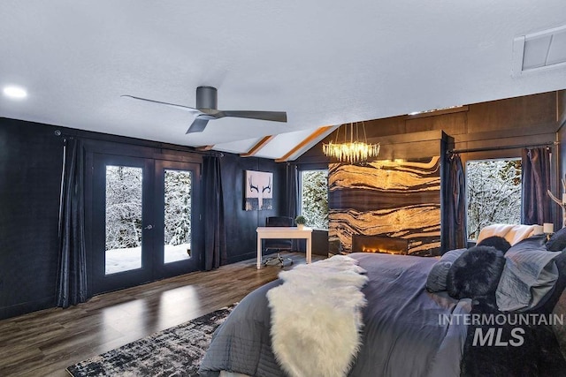 bedroom featuring french doors, wood walls, wood-type flooring, lofted ceiling, and ceiling fan with notable chandelier