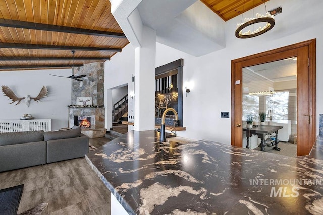 living room featuring hardwood / wood-style flooring, a stone fireplace, wood ceiling, and beamed ceiling