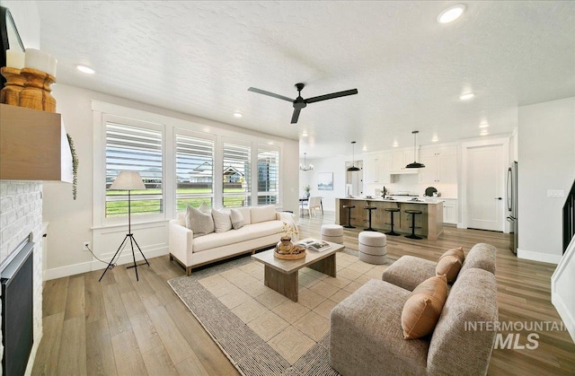 living room with baseboards, ceiling fan, a brick fireplace, and light wood-type flooring