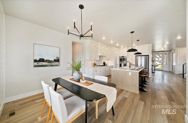 dining room featuring baseboards, an inviting chandelier, light wood-style flooring, and visible vents