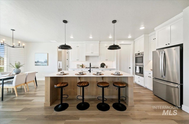 kitchen with an inviting chandelier, white cabinetry, appliances with stainless steel finishes, and a breakfast bar area
