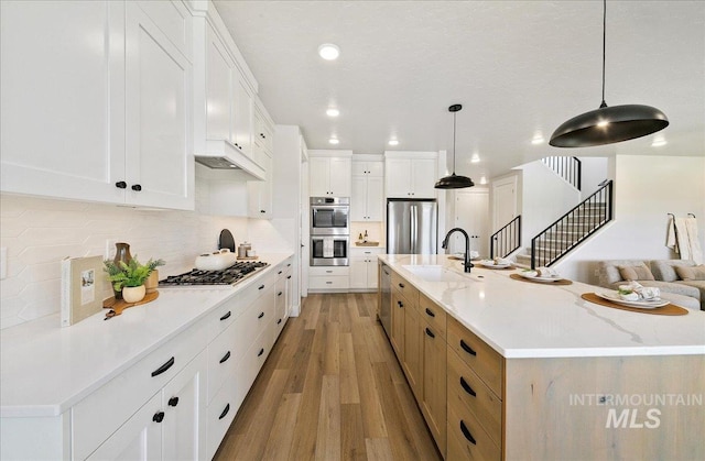 kitchen featuring tasteful backsplash, light wood-type flooring, a sink, open floor plan, and stainless steel appliances