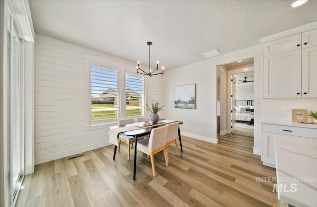dining room with a textured ceiling, visible vents, baseboards, light wood finished floors, and a notable chandelier
