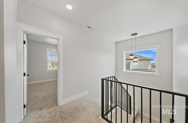 hall with baseboards, visible vents, carpet, and an upstairs landing