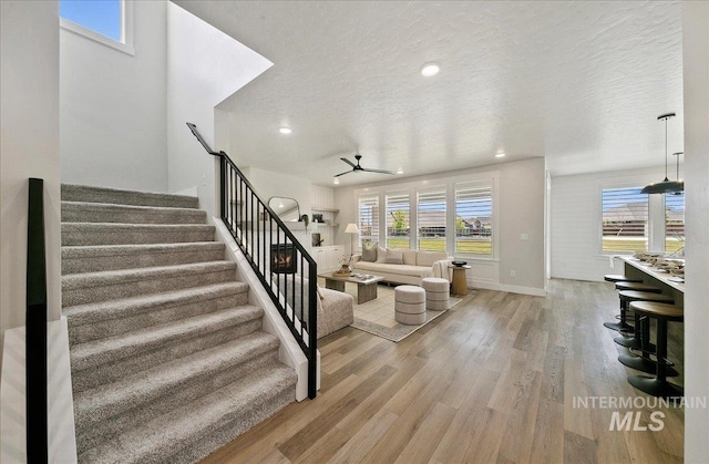 stairway featuring ceiling fan, a textured ceiling, recessed lighting, baseboards, and wood finished floors