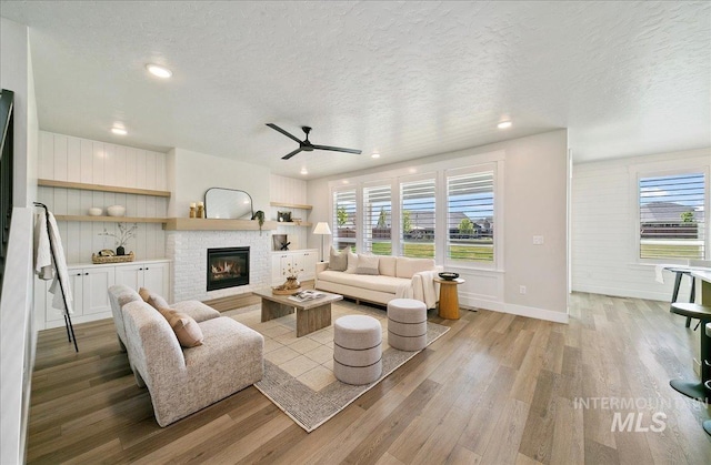 living area with a ceiling fan, a textured ceiling, a glass covered fireplace, and light wood-type flooring
