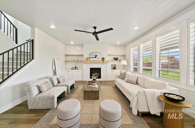 living room featuring stairs, a ceiling fan, a lit fireplace, and wood finished floors