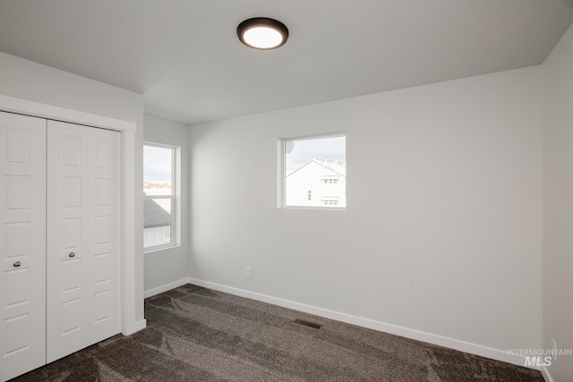 unfurnished bedroom featuring visible vents, baseboards, multiple windows, and dark carpet