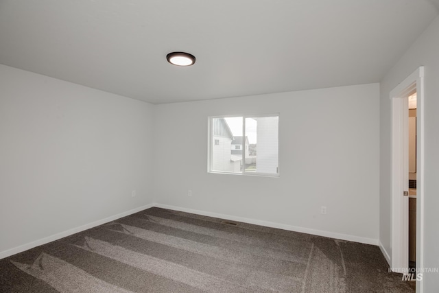 empty room featuring baseboards, visible vents, and dark carpet