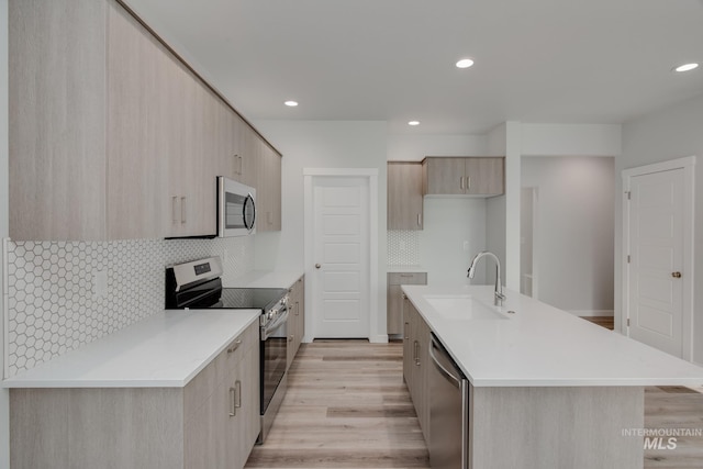kitchen featuring light brown cabinets, modern cabinets, a sink, tasteful backsplash, and appliances with stainless steel finishes