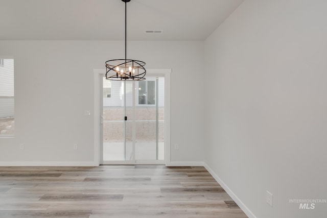 unfurnished dining area with light wood-type flooring, a healthy amount of sunlight, an inviting chandelier, and visible vents