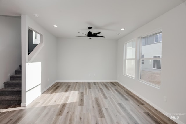 unfurnished living room with a ceiling fan, stairway, and light wood-style flooring