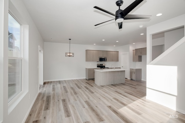 kitchen featuring light wood-style flooring, a center island with sink, modern cabinets, light countertops, and appliances with stainless steel finishes