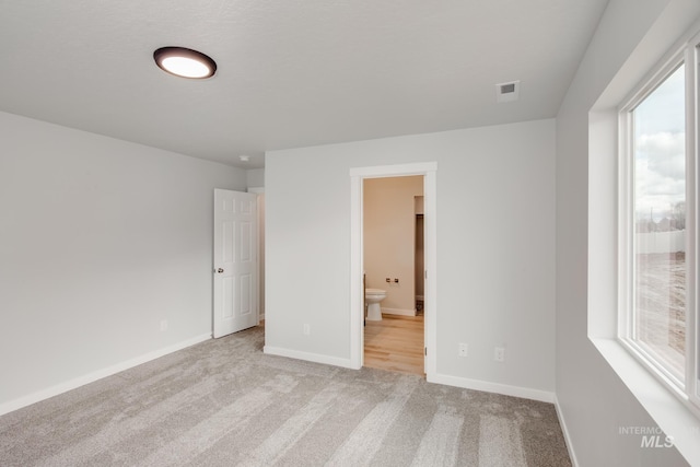 unfurnished bedroom featuring multiple windows, ensuite bathroom, and light carpet