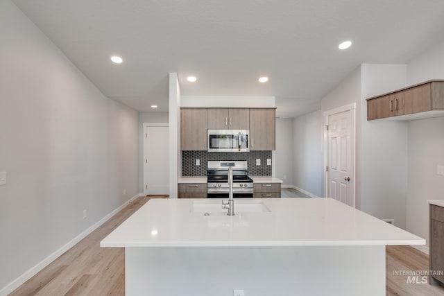 kitchen with a kitchen island with sink, backsplash, light hardwood / wood-style flooring, and appliances with stainless steel finishes