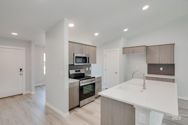 kitchen featuring sink, appliances with stainless steel finishes, tasteful backsplash, an island with sink, and vaulted ceiling