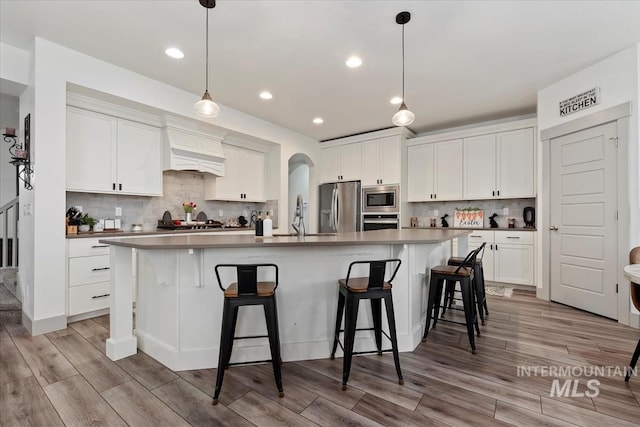 kitchen with white cabinets, light wood-style flooring, a kitchen breakfast bar, and stainless steel appliances