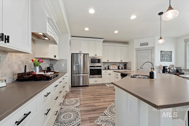 kitchen featuring tasteful backsplash, white cabinets, stainless steel appliances, pendant lighting, and a sink