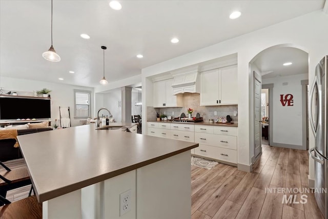 kitchen with white cabinets, a sink, stainless steel appliances, backsplash, and light wood-style flooring
