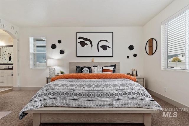 carpeted bedroom with baseboards and arched walkways