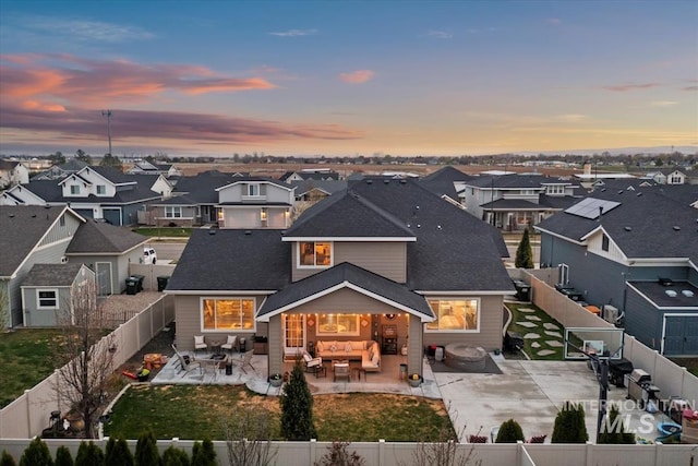 back of house at dusk featuring outdoor lounge area, a patio, a fenced backyard, and a residential view
