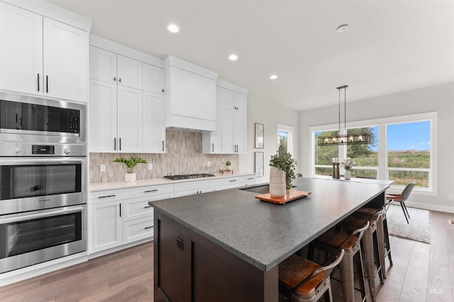 6536 W Flathead Lake St, Eagle, ID 83616 - kitchen featuring stainless steel appliances, a kitchen island, backsplash, wood finished floors, and white cabinetry
