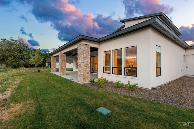 6536 W Flathead Lake St, Eagle, ID 83616 - back of house at dusk with a patio area, stucco siding, and a lawn