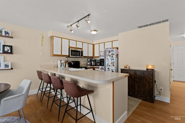 kitchen featuring white refrigerator with ice dispenser, light wood finished floors, stainless steel microwave, visible vents, and black range with electric stovetop