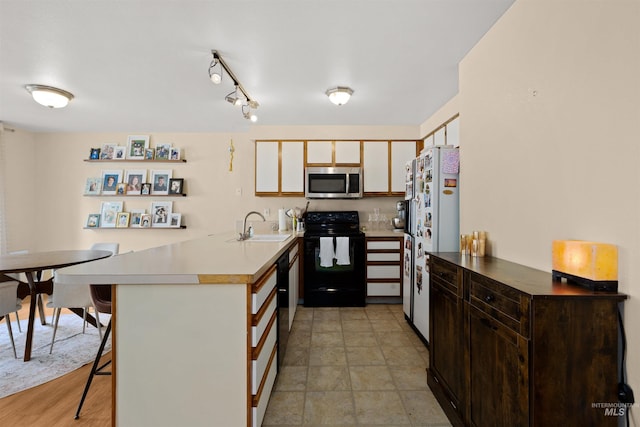 kitchen featuring freestanding refrigerator, a peninsula, stainless steel microwave, black range with electric stovetop, and a sink