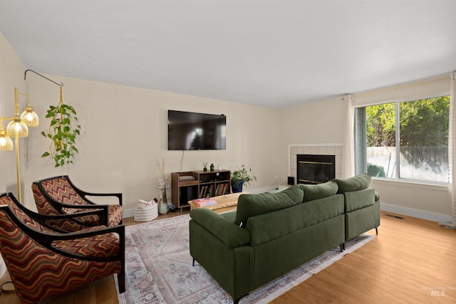 living room featuring baseboards, a tile fireplace, visible vents, and light wood-style floors