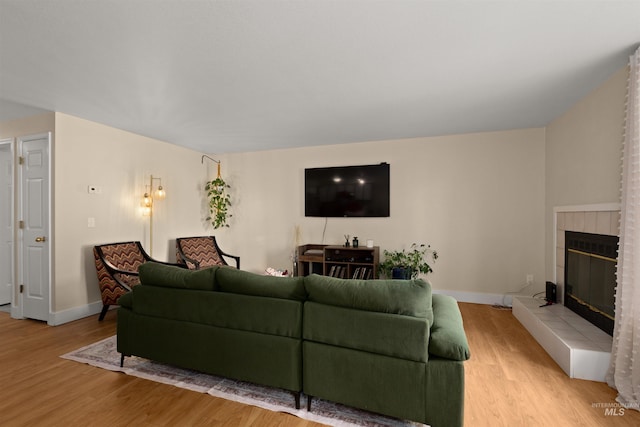 living room featuring light wood-type flooring, baseboards, and a tiled fireplace