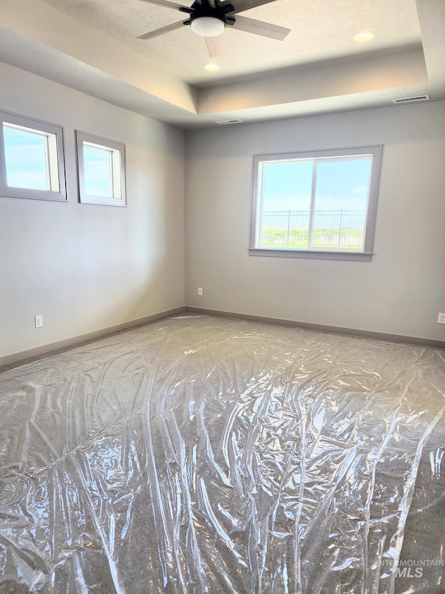 empty room with visible vents, a raised ceiling, a healthy amount of sunlight, and ceiling fan