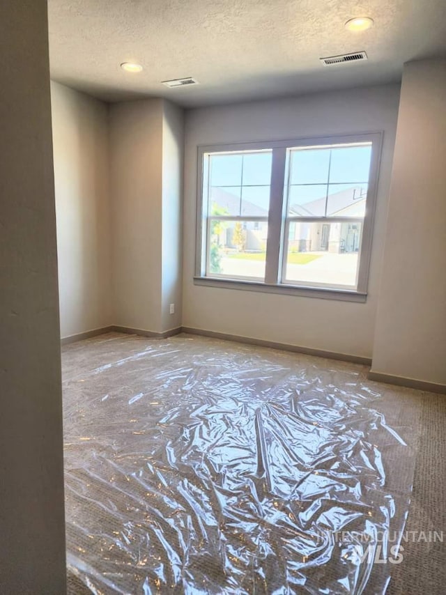 empty room with recessed lighting, a textured ceiling, visible vents, and baseboards