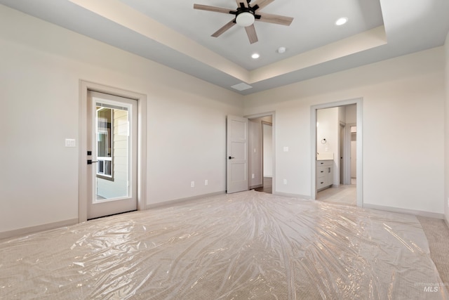 unfurnished bedroom featuring recessed lighting, a raised ceiling, baseboards, light colored carpet, and ensuite bathroom