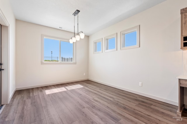 unfurnished dining area featuring baseboards, visible vents, wood finished floors, and a healthy amount of sunlight