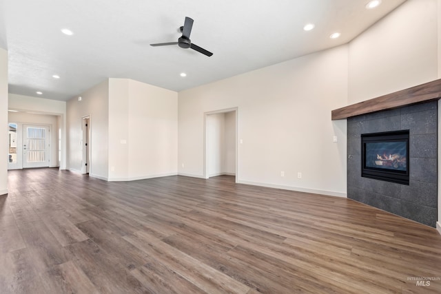 unfurnished living room featuring baseboards, recessed lighting, wood finished floors, a tiled fireplace, and a ceiling fan