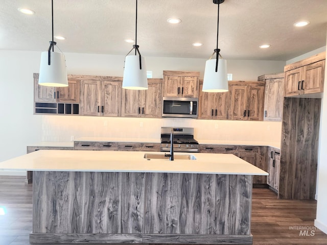 kitchen with recessed lighting, a kitchen island with sink, appliances with stainless steel finishes, light countertops, and dark wood-style flooring
