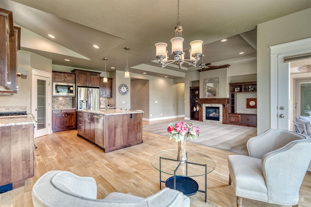 living area with recessed lighting, light wood-style floors, baseboards, a glass covered fireplace, and a notable chandelier