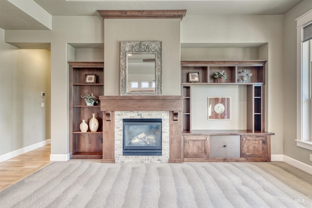 unfurnished living room featuring built in shelves, a glass covered fireplace, carpet flooring, and baseboards