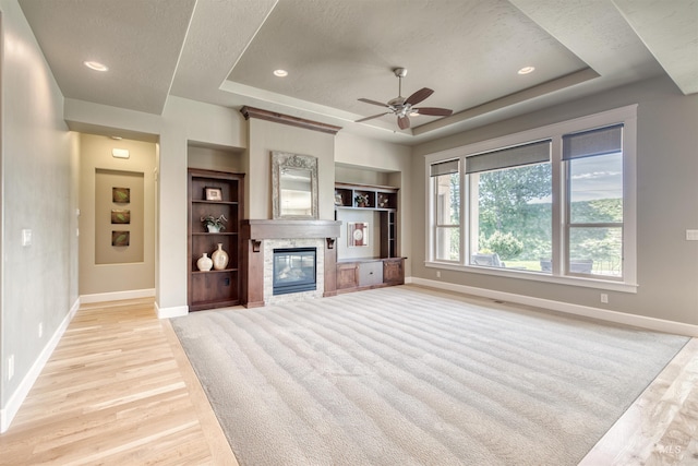 unfurnished living room with light wood-type flooring, baseboards, and a raised ceiling