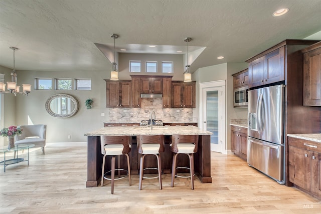 kitchen featuring stainless steel appliances, light wood-style flooring, a textured ceiling, baseboards, and decorative backsplash