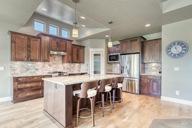 kitchen with a sink, an island with sink, stainless steel appliances, light wood finished floors, and under cabinet range hood
