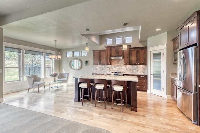 kitchen with a textured ceiling, light wood-type flooring, stainless steel fridge with ice dispenser, a breakfast bar, and under cabinet range hood