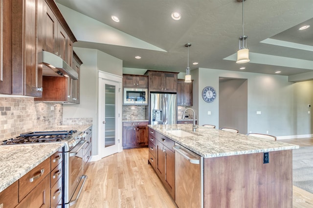 kitchen with light stone counters, a sink, appliances with stainless steel finishes, light wood-style flooring, and under cabinet range hood