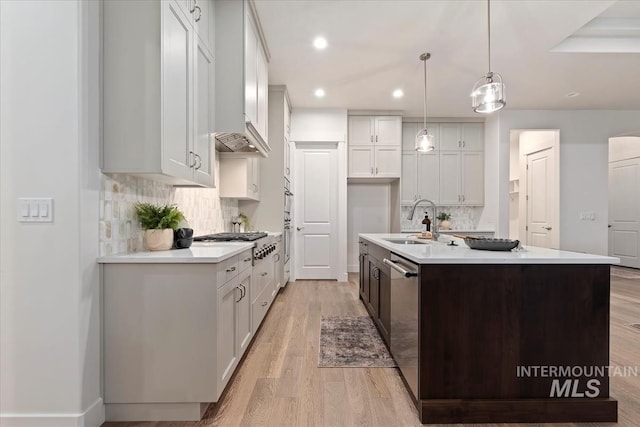 kitchen featuring an island with sink, sink, white cabinets, and hanging light fixtures