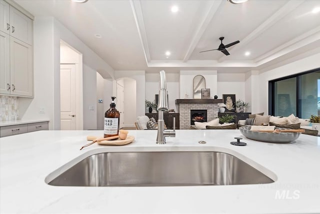 kitchen with a brick fireplace, sink, ceiling fan, gray cabinets, and beam ceiling