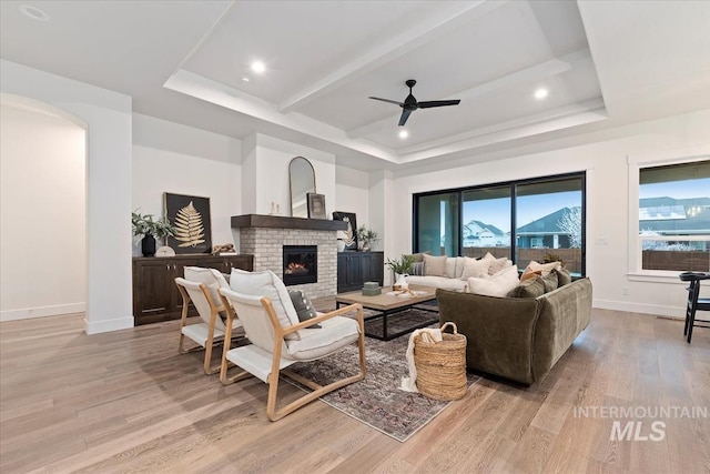 living room with light wood-type flooring, ceiling fan, a brick fireplace, and a wealth of natural light