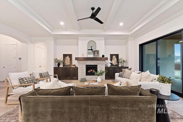 living room with hardwood / wood-style flooring, a brick fireplace, ceiling fan, and beam ceiling